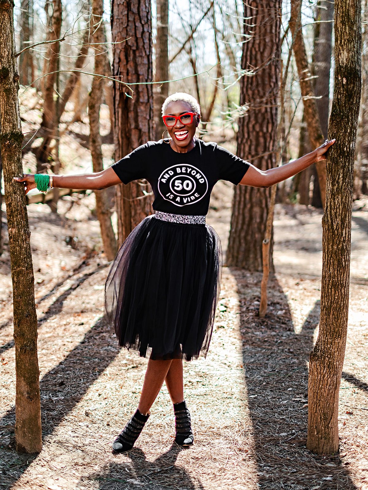 Kwavi in a black tutu and red glasses, arms wide, laughing